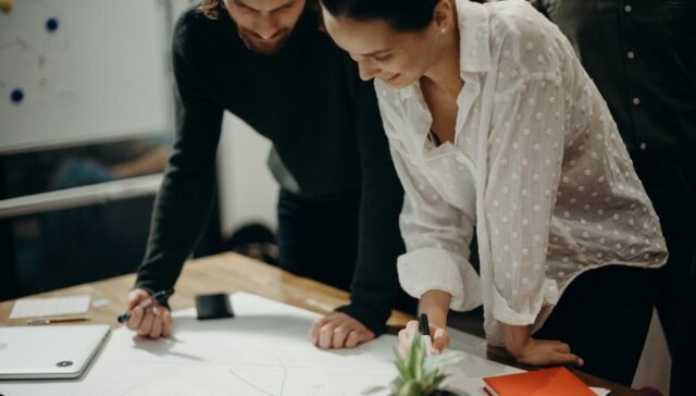 Man and Woman Leaning on Table Staring at White Board on Top of Table Having a Meeting